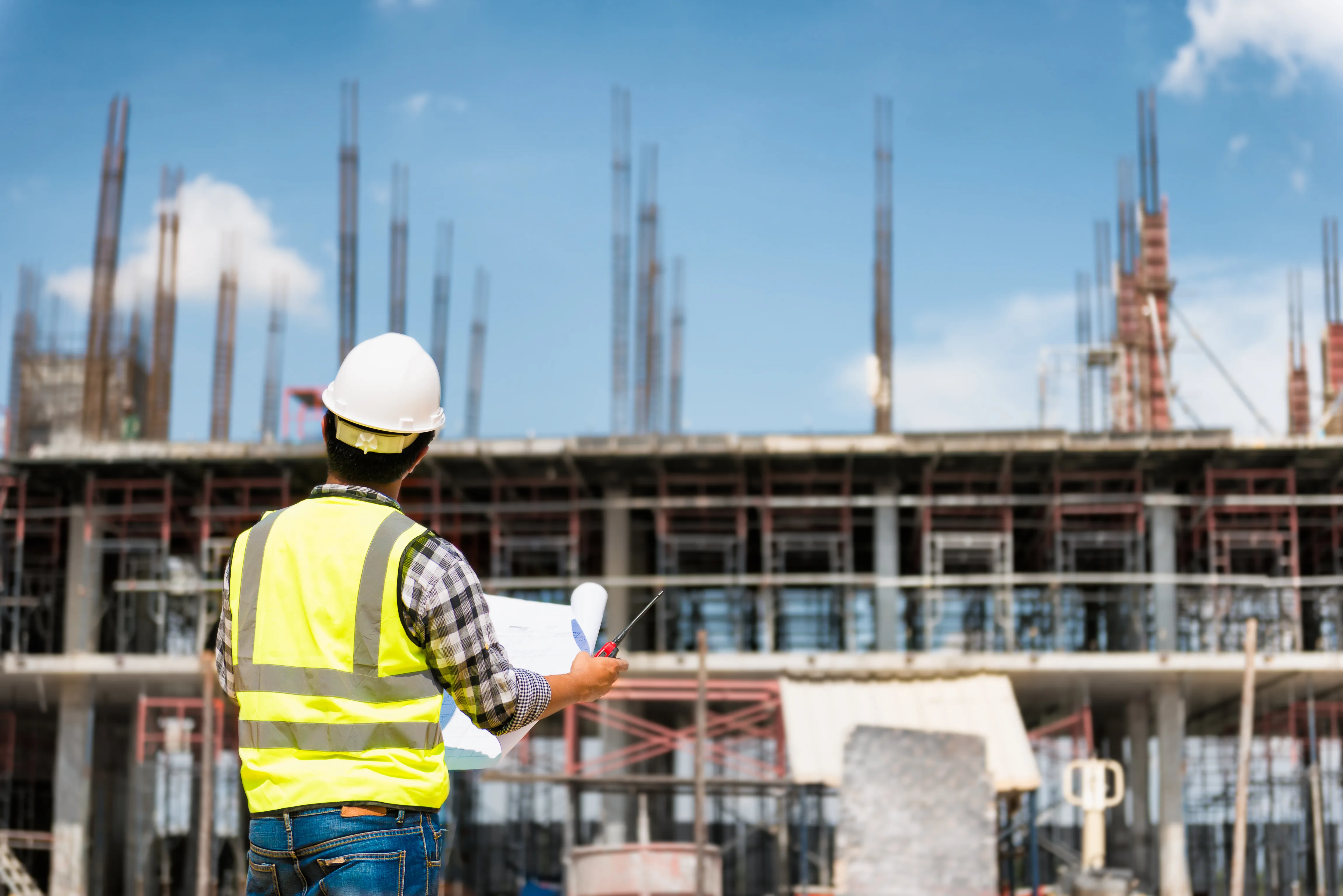 Uomo con un disegno tecnico in mano che osserva un cantiere con un palazzo in costruzione